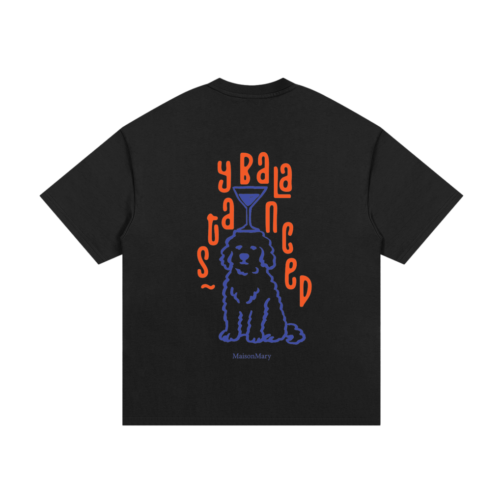 A black short-sleeve t-shirt with a graphic print on the front. The graphic features a blue outline of a dog sitting underneath orange text that reads STAYBALANCED