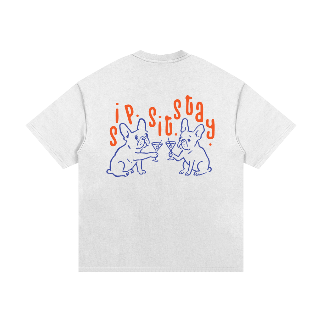 A white short-sleeve t-shirt shown from the back, featuring a graphic print of two blue line-art French bulldogs clinking martini glasses under orange text that reads sip.sit.stay